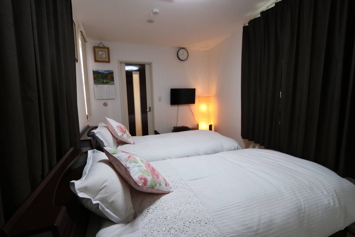 A hotel room with two beds, a bedside table, a clock, a TV, and a calendar on the wall.