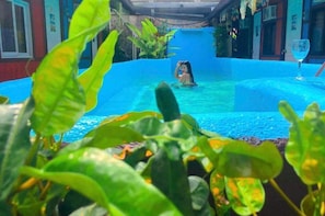 Une zone de piscine avec une personne dans l’eau, entourée de verdure et bordée d’une piscine bleue.