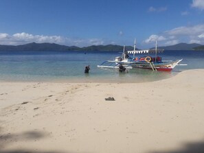 A boat on a beach with clear water and mountains in the background. - El Nido Hostel Sun Valley (El Nido)