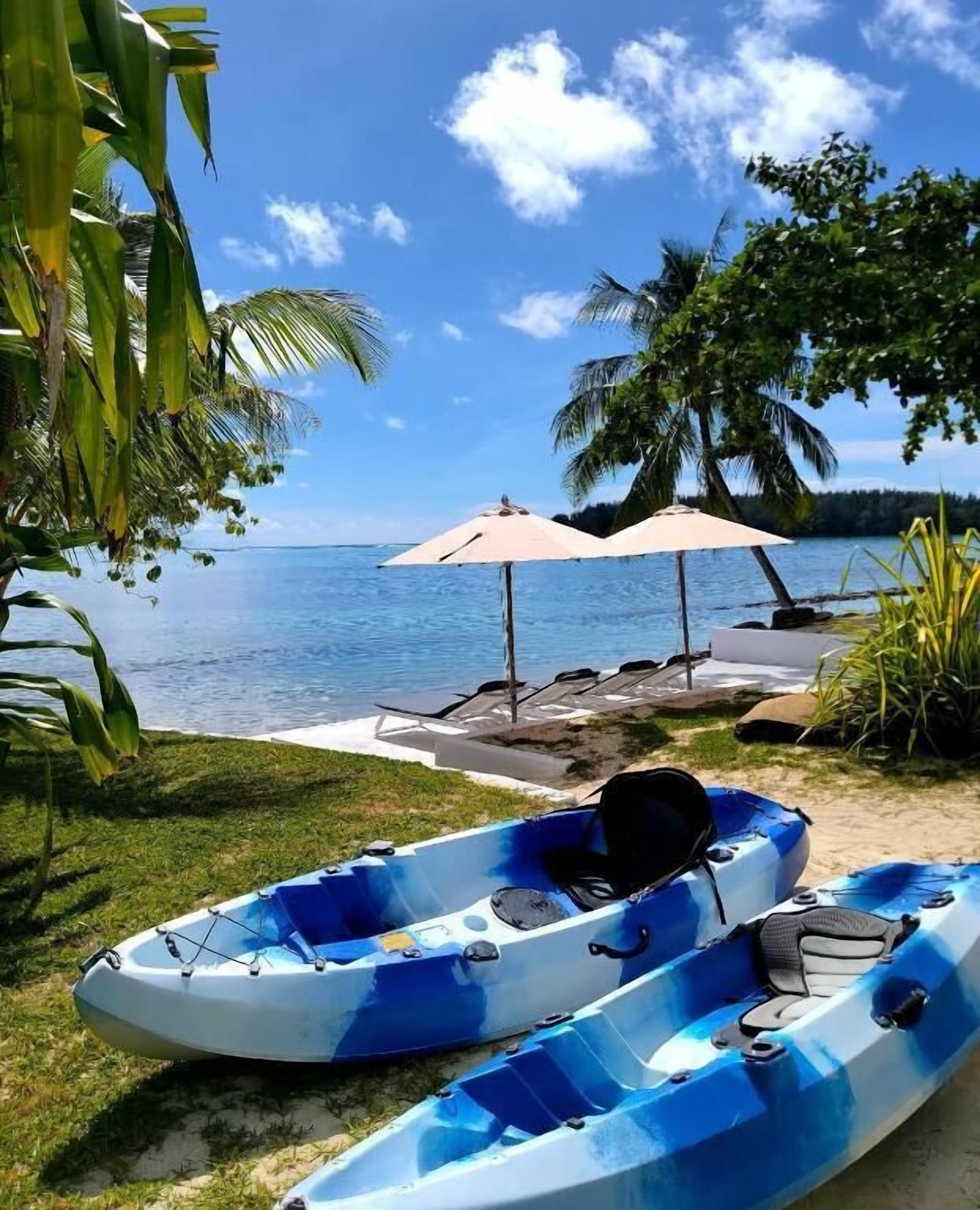 Deux kayaks bleus sont posés sur une pelouse, d’où l’on a une vue sur l’océan et les palmiers.