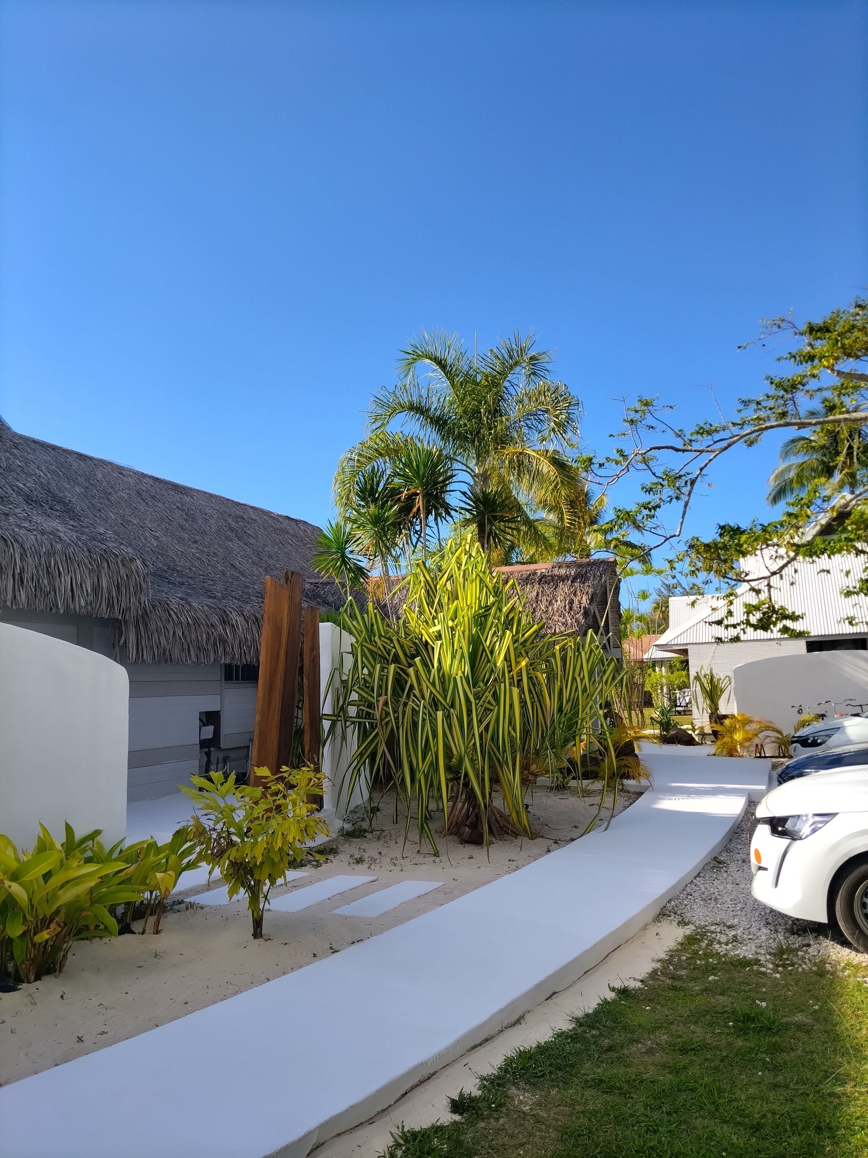 Un resort con un edificio de techo de paja, una estructura blanca y un coche blanco estacionado cerca.