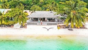 Un resort sulla spiaggia con un edificio a tetto di paglia, palme e vista libera sull'oceano.
