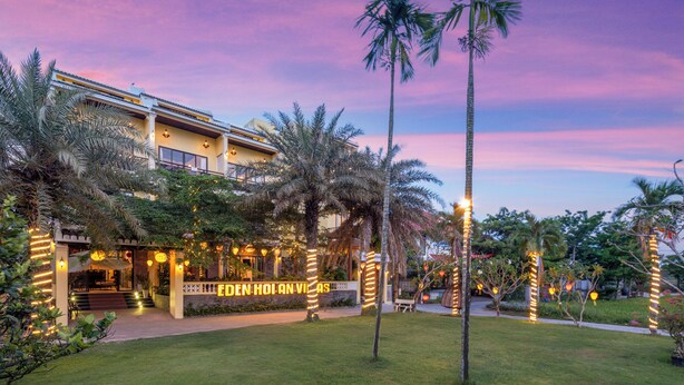 Un hotel con una entrada bien iluminada, palmeras y un letrero que dice "EDEN HOLAN VILLAS".