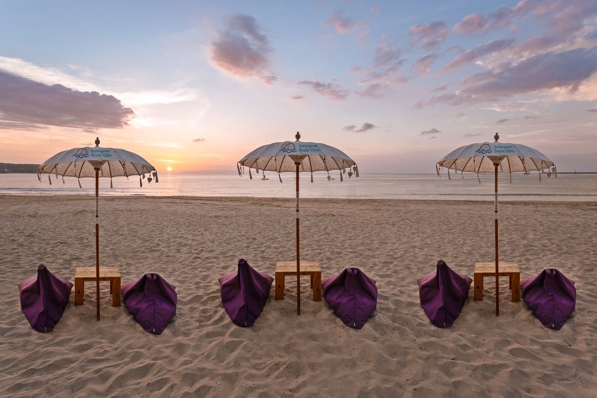 Beach umbrellas and chairs lined up on a sandy beach with a sunset in the background.