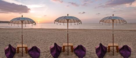 Beach umbrellas and chairs lined up on a sandy beach with a sunset in the background.