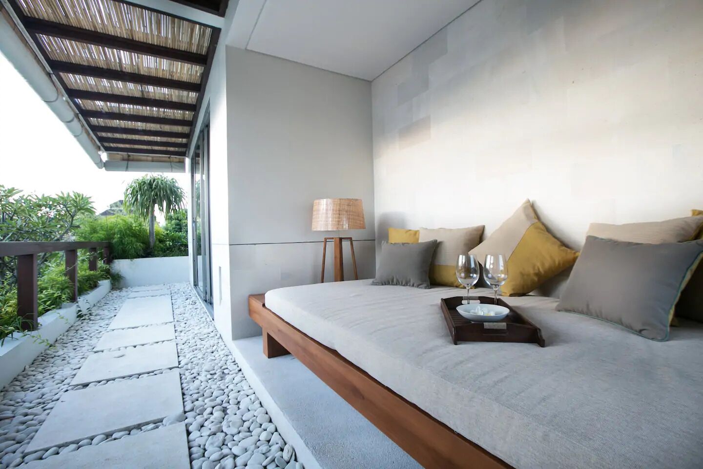 A modern bedroom with a large bed, a bedside table with a lamp, and a tray with glasses and a bottle.