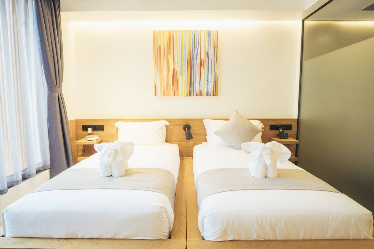 A hotel room with two beds, a wooden headboard, a wall-mounted artwork, and a nightstand with a phone and a lamp.