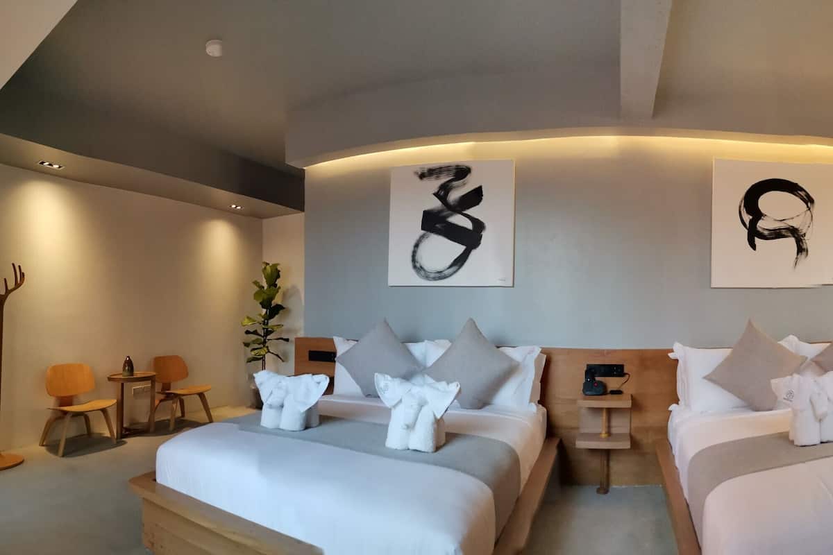 A modern hotel room with two beds, a desk, and a seating area.