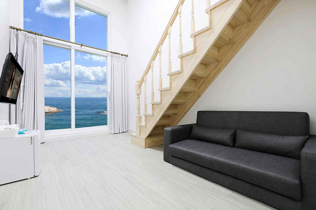 Ein modernes Wohnzimmer mit einem großen Fenster, einem grauen Sofa und einer Holztreppe.