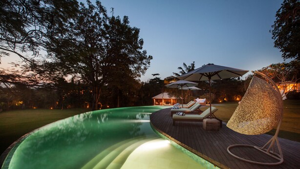 A swimming pool with a wooden deck, lounge chairs, and umbrellas.
