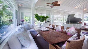A spacious living area with a wooden dining table, wicker chairs, and a white sofa with floral cushions.