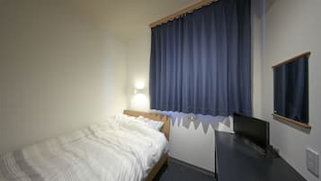 A bedroom with a bed, a desk, a chair, a lamp, and a window with curtains.