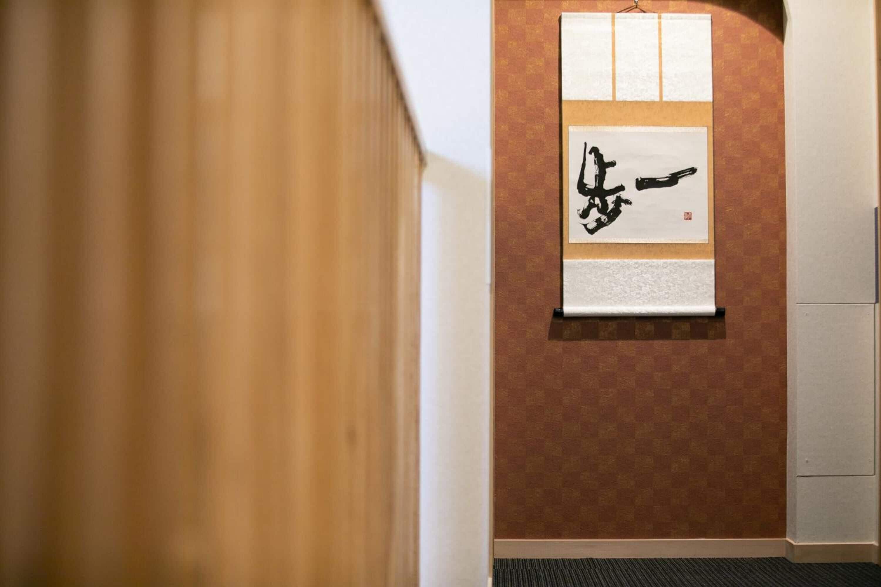 A hallway with a wooden door, a wall-mounted artwork with calligraphy, and a patterned wall.