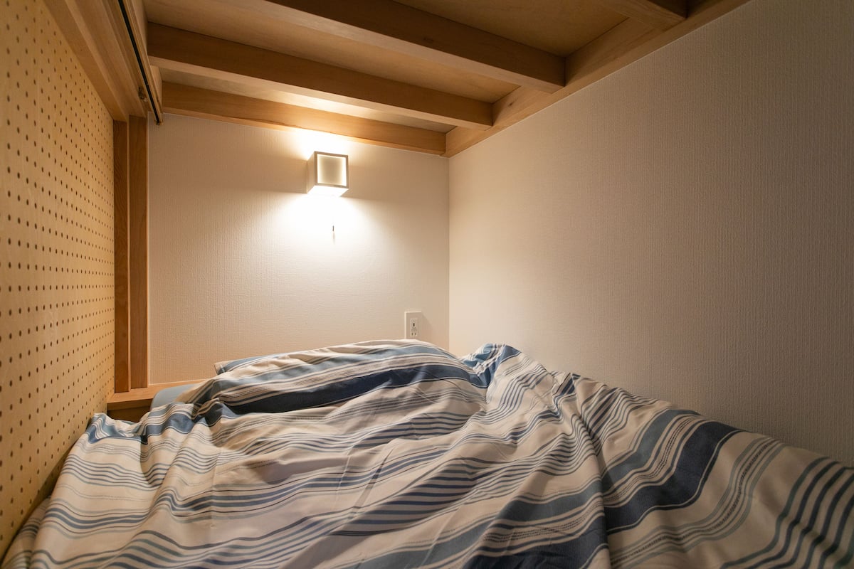 Un dormitorio con cama, una lámpara fijada a la pared y una viga de techo de madera.