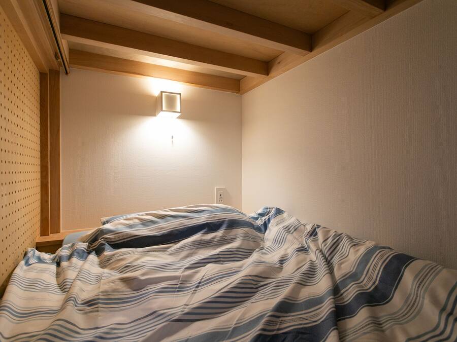 A bedroom with a bed, a wall-mounted light, and a wooden ceiling beam.