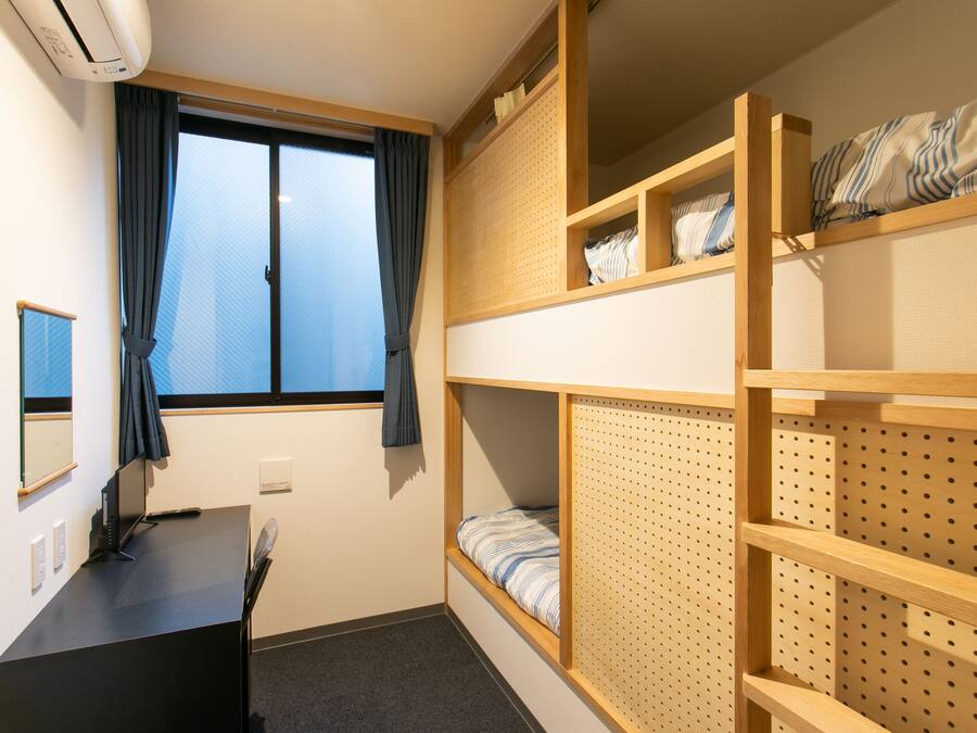 A compact room with bunk beds, a desk, and a window with curtains.