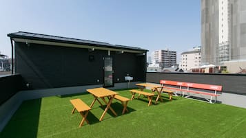 Una terraza en la azotea con césped artificial, mesas de picnic de madera y un pequeño edificio de fachada negra.