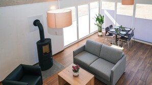 Uma sala de estar moderna com uma lareira a lenha preta, sofá cinzento e uma mesa de centro de madeira com um vaso de flores.