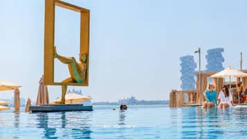 A pool area with a large golden frame sculpture, a person performing an acrobatic pose, and a cityscape in the background.