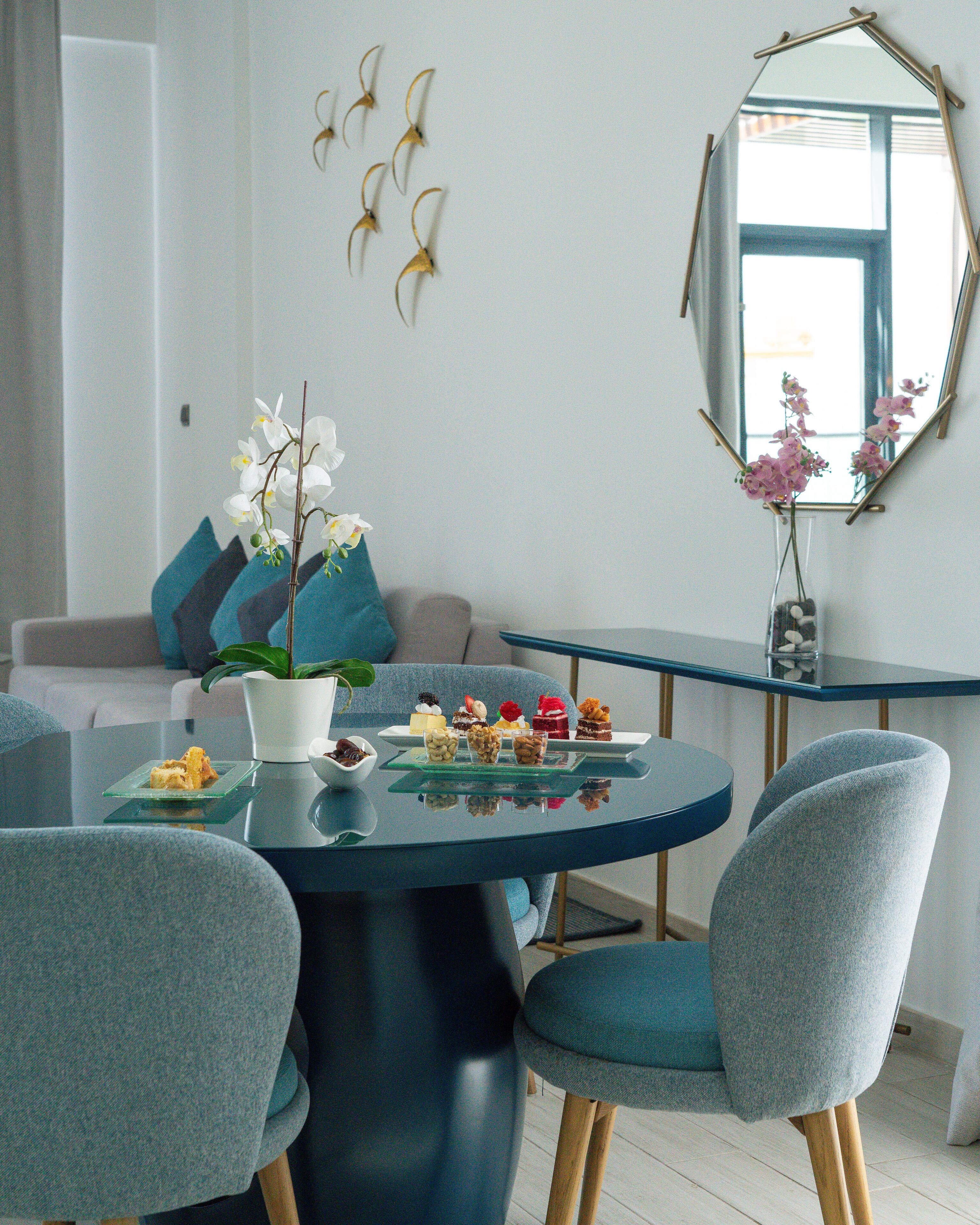 Een eetgedeelte met een ronde tafel, stoelen, een vaas met bloemen en een spiegel aan de muur.
