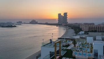 A rooftop terrace with a view of the sea and sunset, featuring modern architecture and outdoor seating.