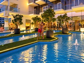 A modern hotel with a swimming pool, indoor plants, and a well-lit lounge area.