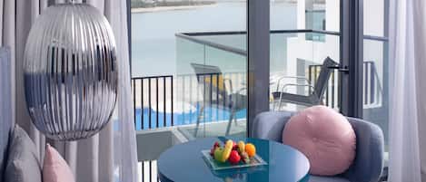 Una habitación moderna con balaustrada de vidrio, una mesa redonda con fruta y vista al mar.