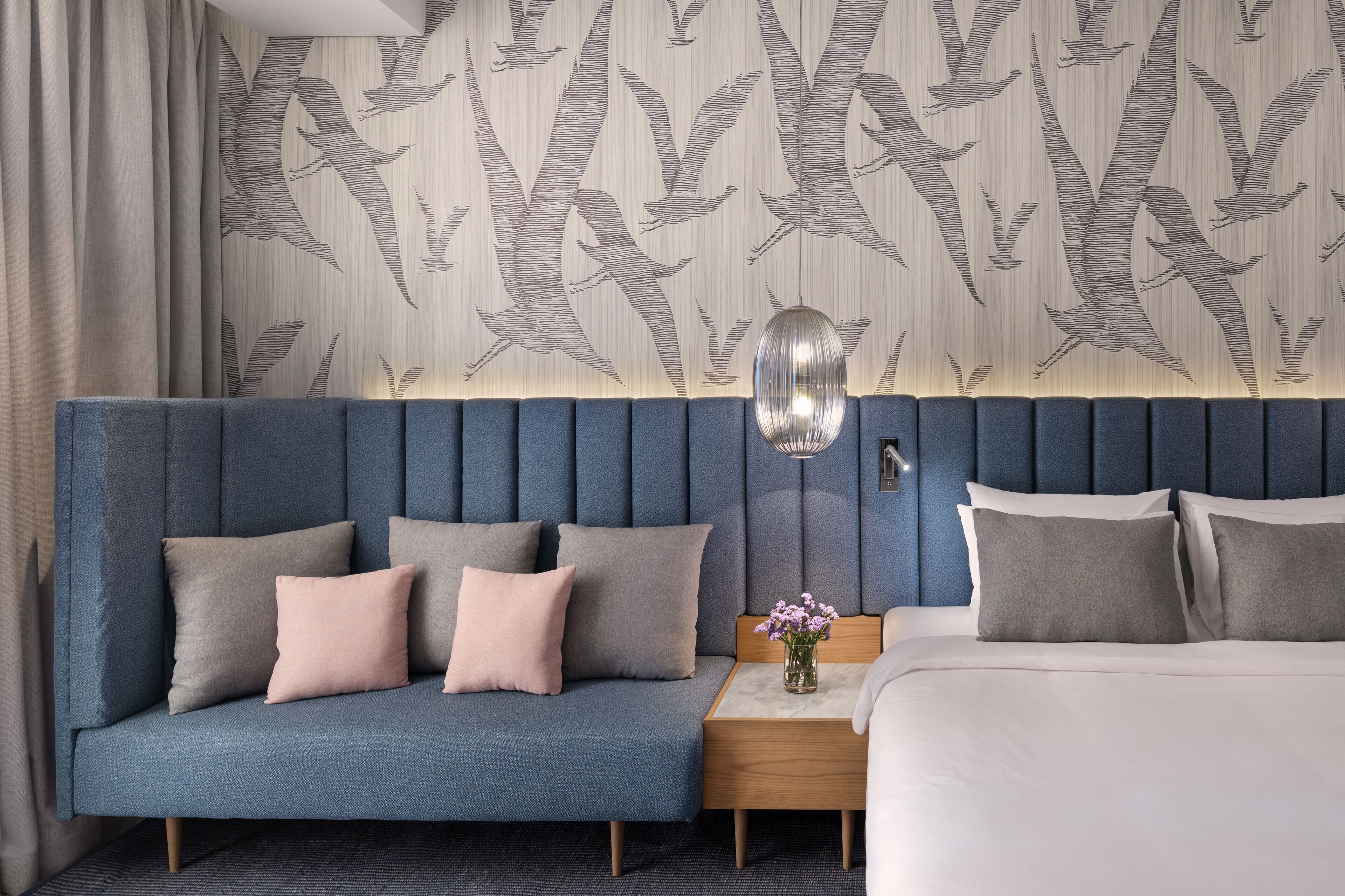 A hotel room with a blue sofa, a wooden nightstand, and a bed.