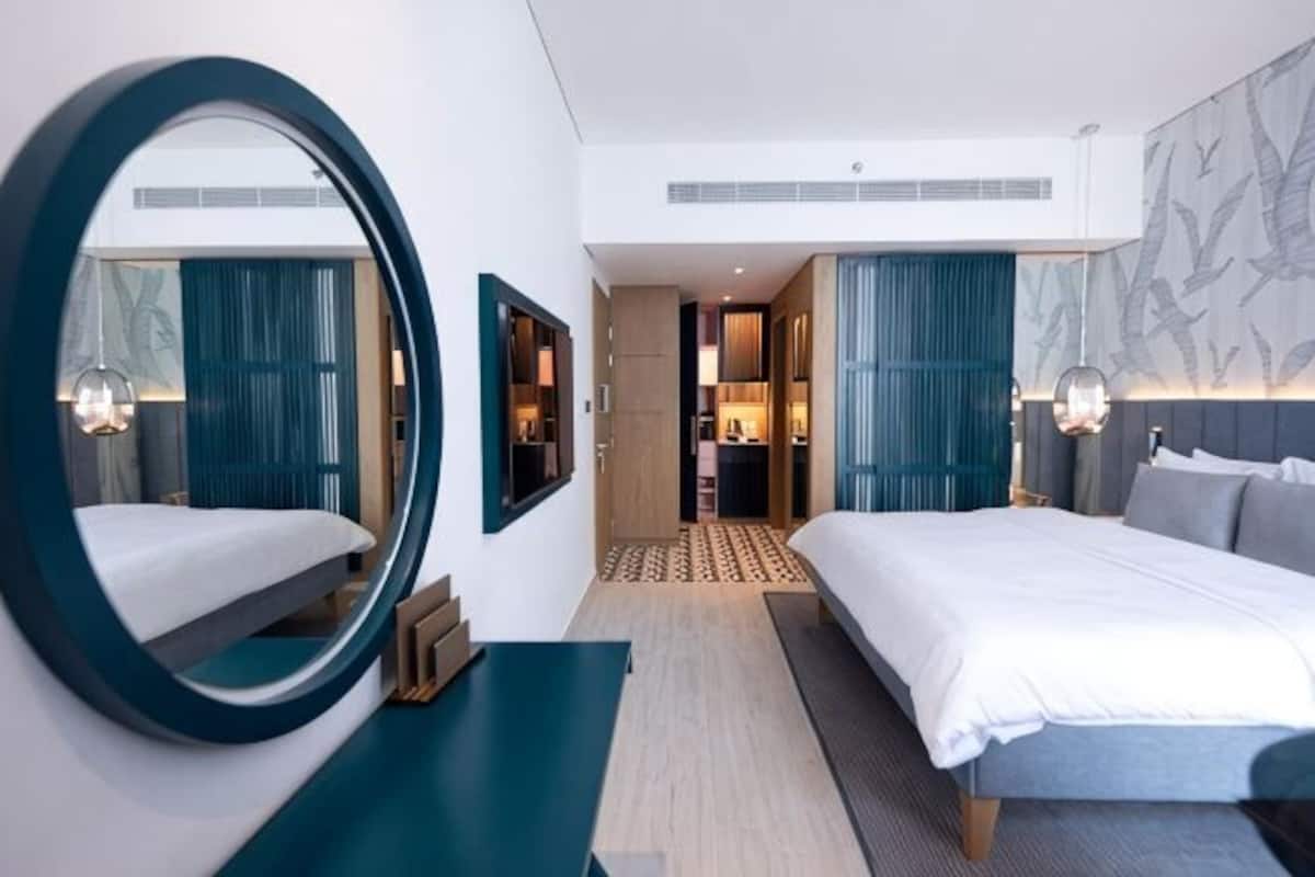 Une chambre dâhĂŽtel moderne avec un grand lit, un miroir rond, un bureau et une vue sur la piĂšce.