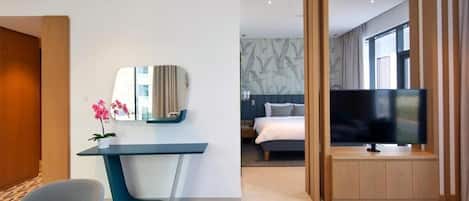A modern hotel room with a desk, chair, TV, and a bed with a headboard.