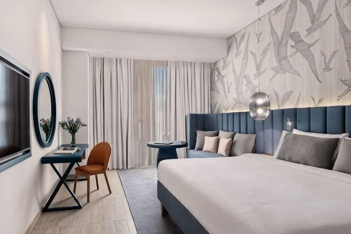 Une chambre d’hôtel avec un grand lit, un bureau, une chaise, une télévision et un mur décoré d’un motif.