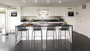 Une cuisine moderne avec des meubles blancs, un îlot central doté de tabourets et des appareils électroménagers intégrés.