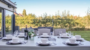 Un espace de restauration en plein air avec une table dressée pour quatre personnes, agrémentée de bols, d’assiettes et de verres à vin blancs.