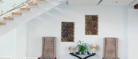 A modern lobby with a staircase, two armchairs, a glass coffee table, and decorative wall art.