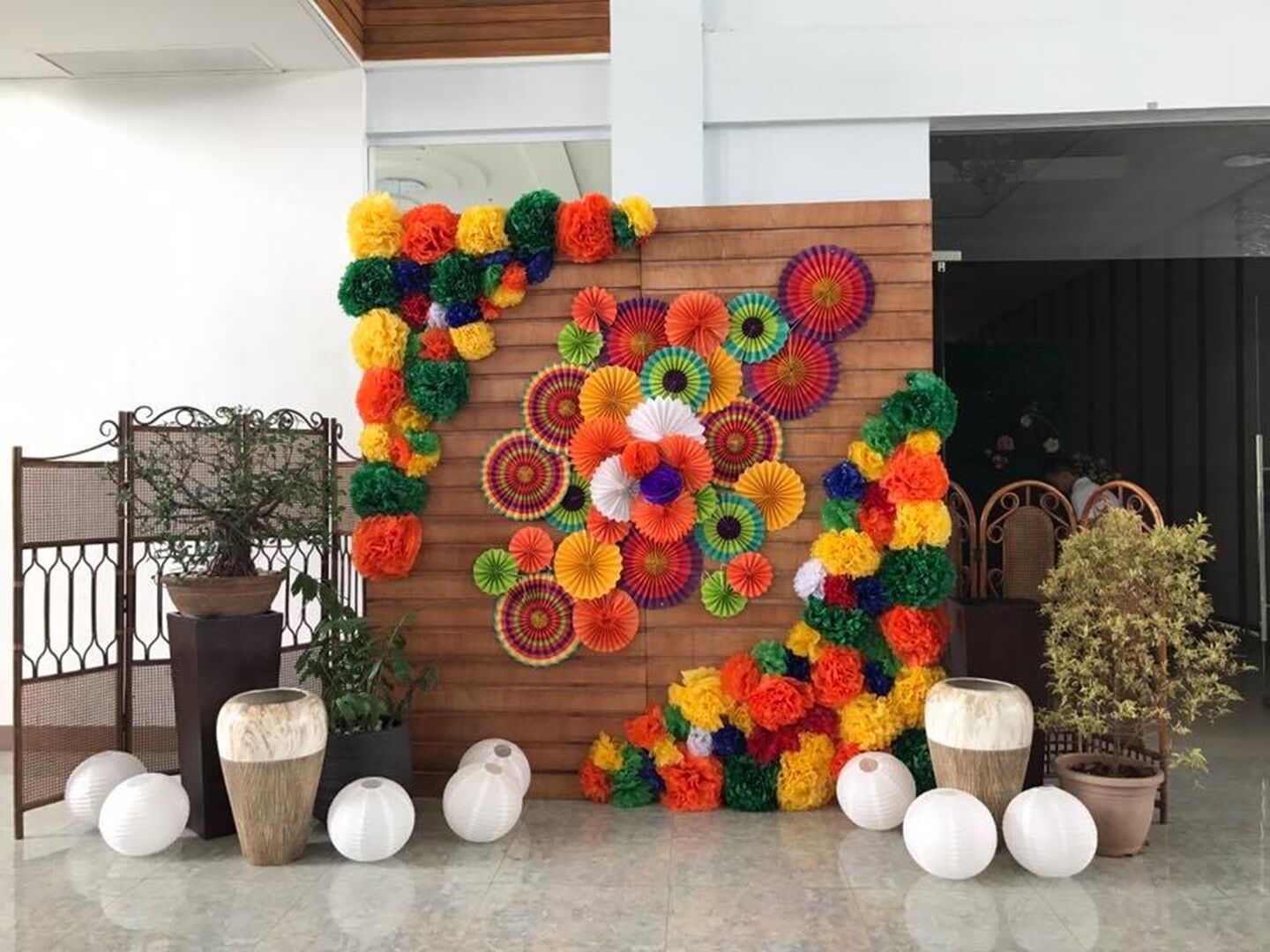 A decorative wall with colorful paper flowers and a potted plant.