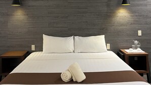 Una habitación de hotel moderna con una cama grande, dos mesitas de noche, un cabecero de madera y dos lámparas colgantes.