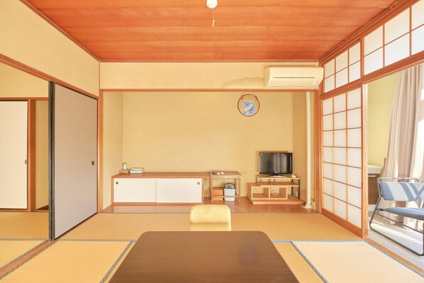 Una habitación japonesa tradicional con suelo de tatami, una mesa baja, un televisor y puertas correderas.