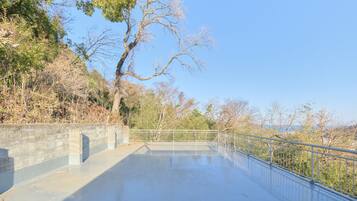 A concrete viewing platform with a metal railing, surrounded by trees and a clear sky.