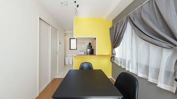 A compact room with a dining table, chairs, a kitchenette, and a window with curtains.