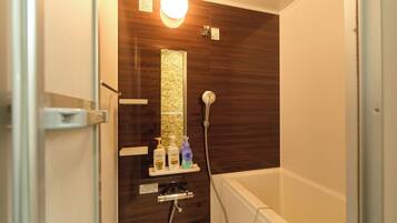 A bathroom with a shower, a glass door, a light fixture, and a shelf with toiletries.