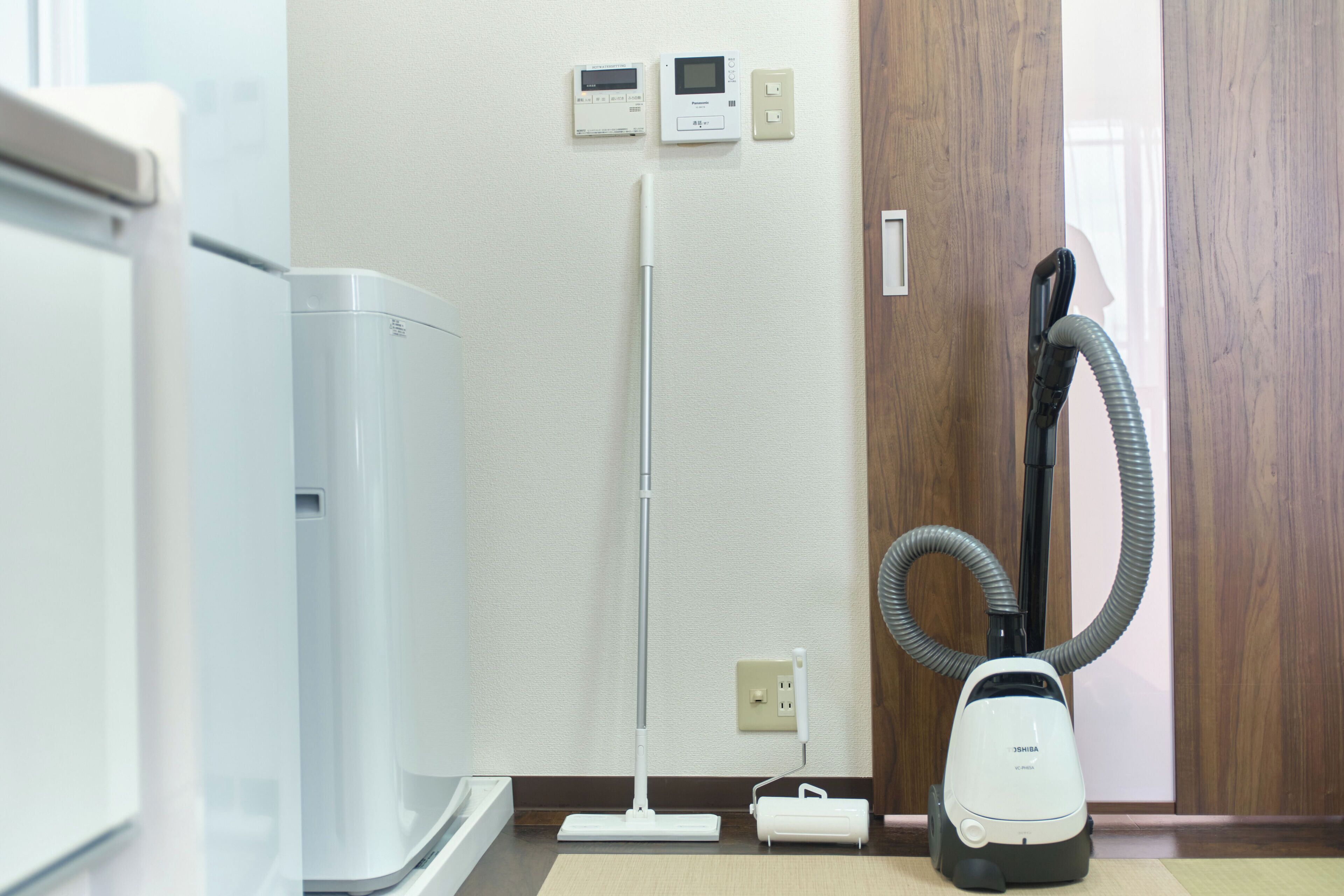A room with a white air purifier, a standing vacuum cleaner, and a vacuum cleaner with a hose.