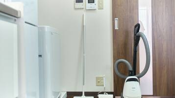 A room with a white air purifier, a standing vacuum cleaner, and a vacuum cleaner with a hose.