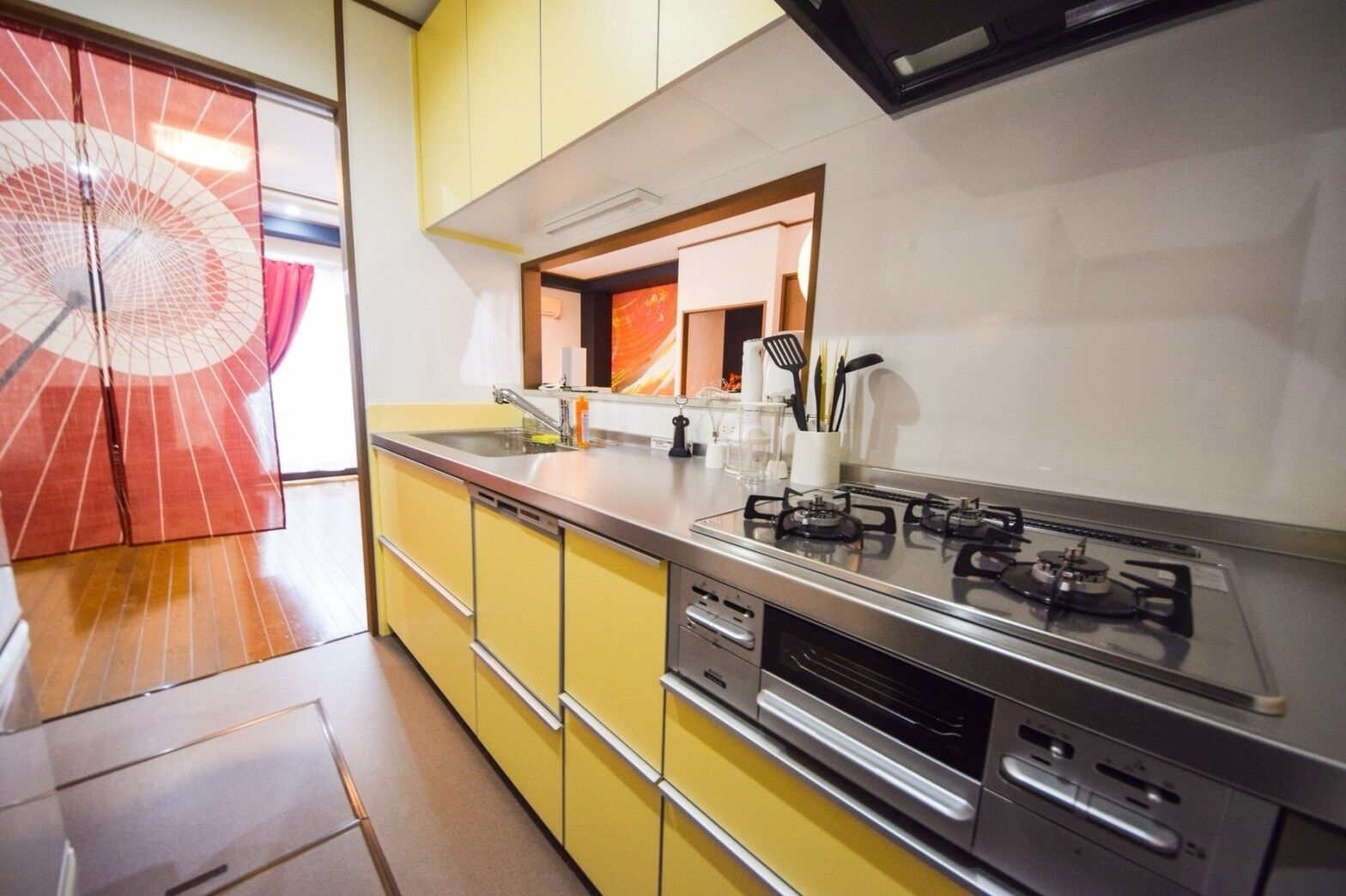 A modern kitchen with yellow cabinets, a stainless steel stove, and a large window with a view of a red umbrella.