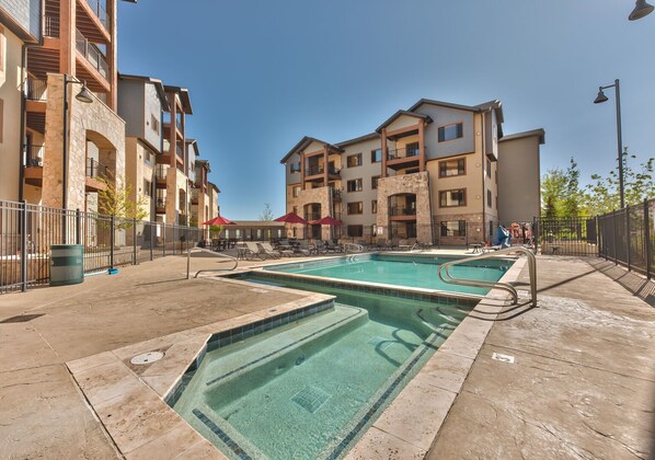 A pool area with two swimming pools, lounge chairs, and a building with balconies. - Step out the door and on the Canyons Village Skyway Gondola - Pool, Sauna, Steam Room Mountain Views (Park City)