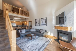 Amplia sala de estar con un sofá modular grande, chimenea, televisión montada en la pared y una cocina al fondo.