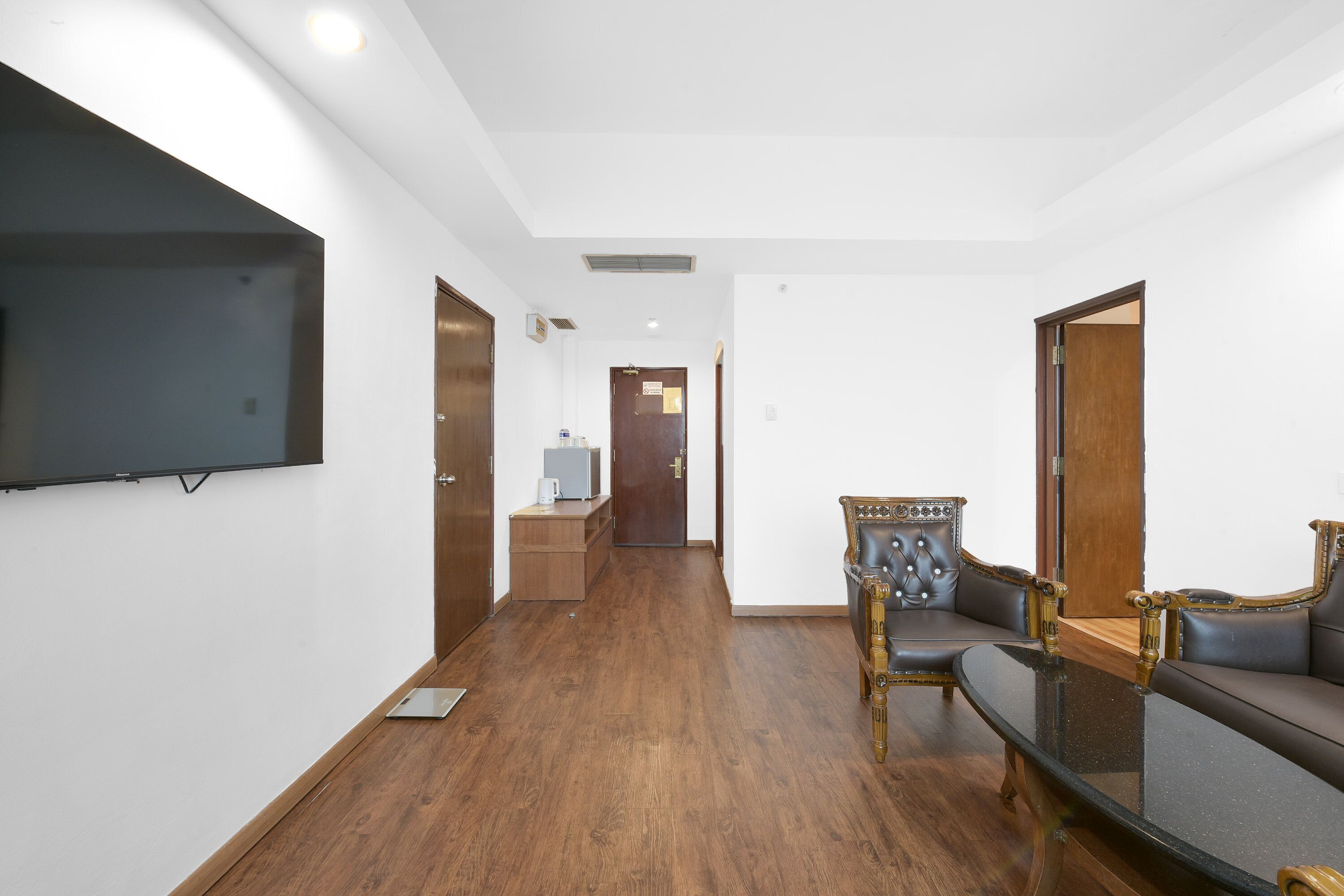 Habitación de hotel con televisión de pantalla plana montada en la pared, suelo de madera, sofá y sillón con detalles ornamentales.