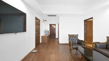 Habitación de hotel con televisión de pantalla plana montada en la pared, suelo de madera, sofá y sillón con detalles ornamentales.