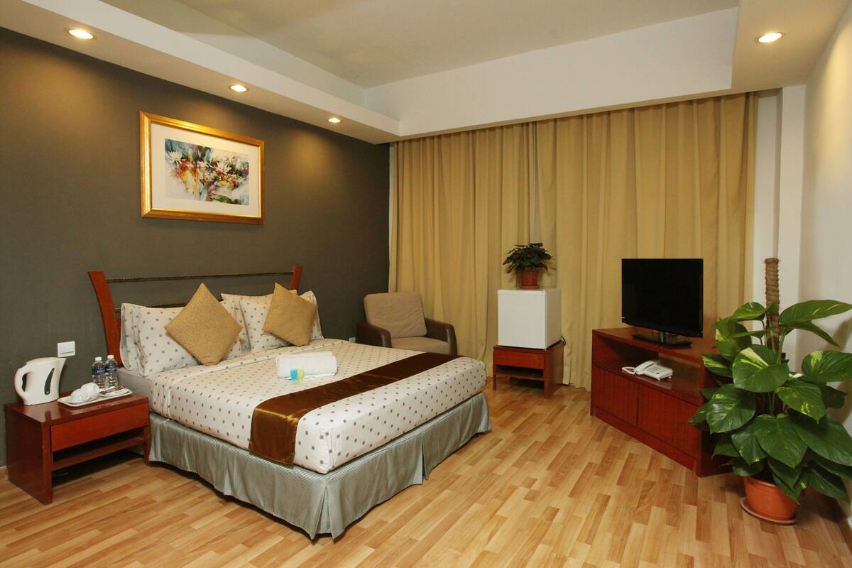 A hotel room with a bed, a television, a plant, a desk, and a painting on the wall.