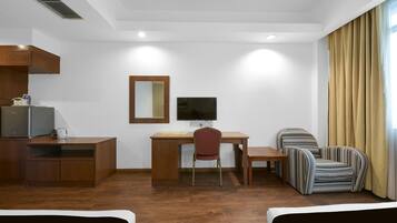 A hotel room with a wooden desk, a computer, a TV, a striped armchair, and a bed.