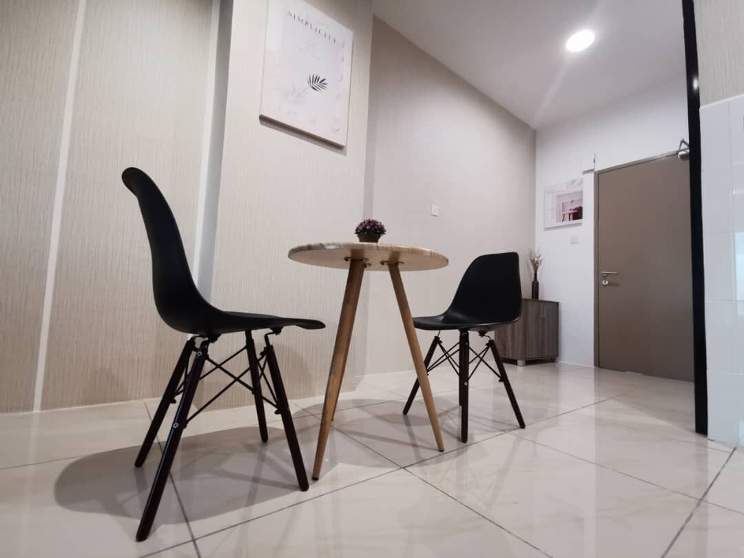 A modern dining area with two black chairs and a round wooden table.